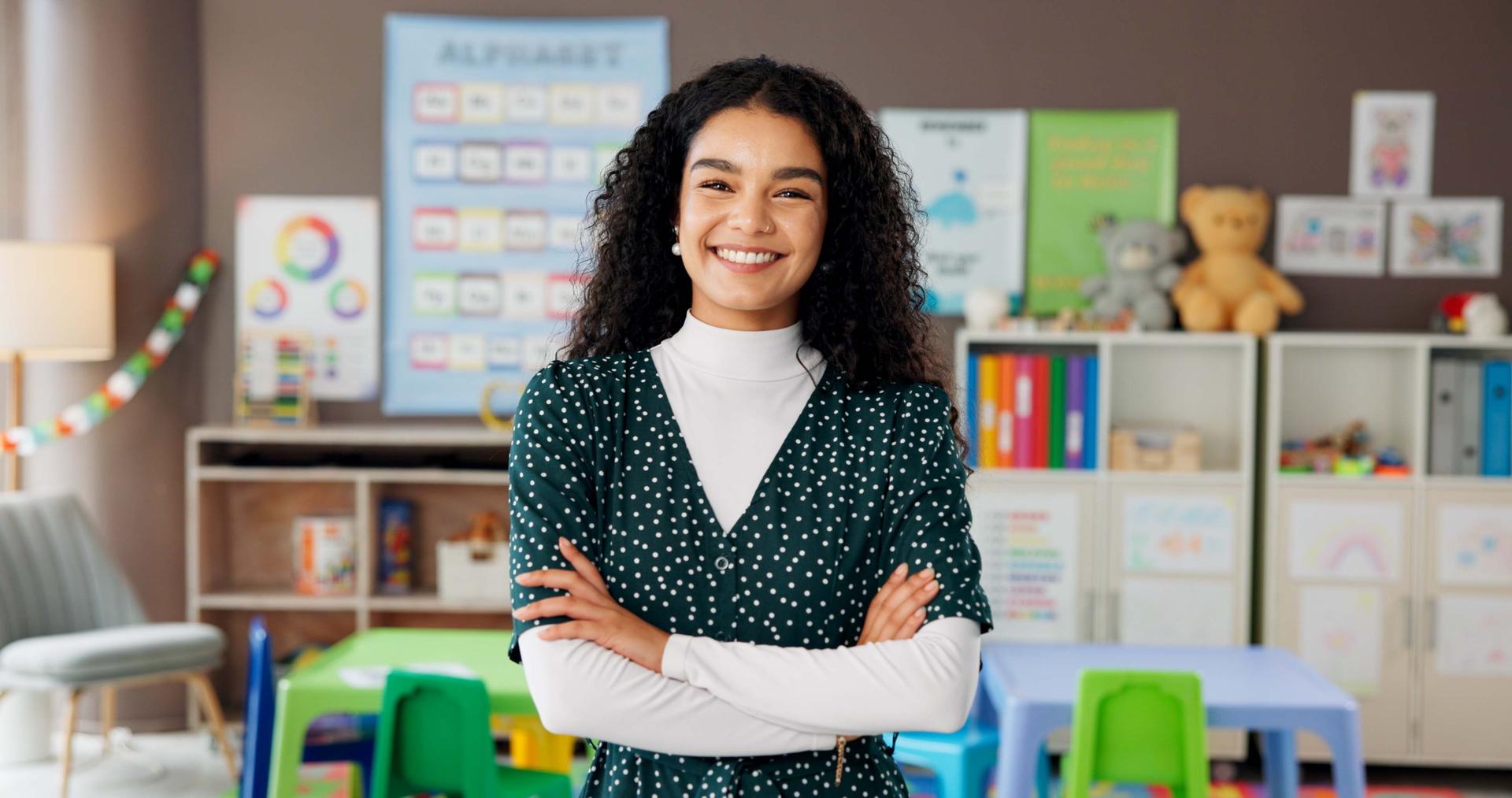 Woman, teacher and portrait in classroom with confidence, smile and montessori about us. Educator, kindergarten and arms crossed in school for education, career pride or faculty member with passion