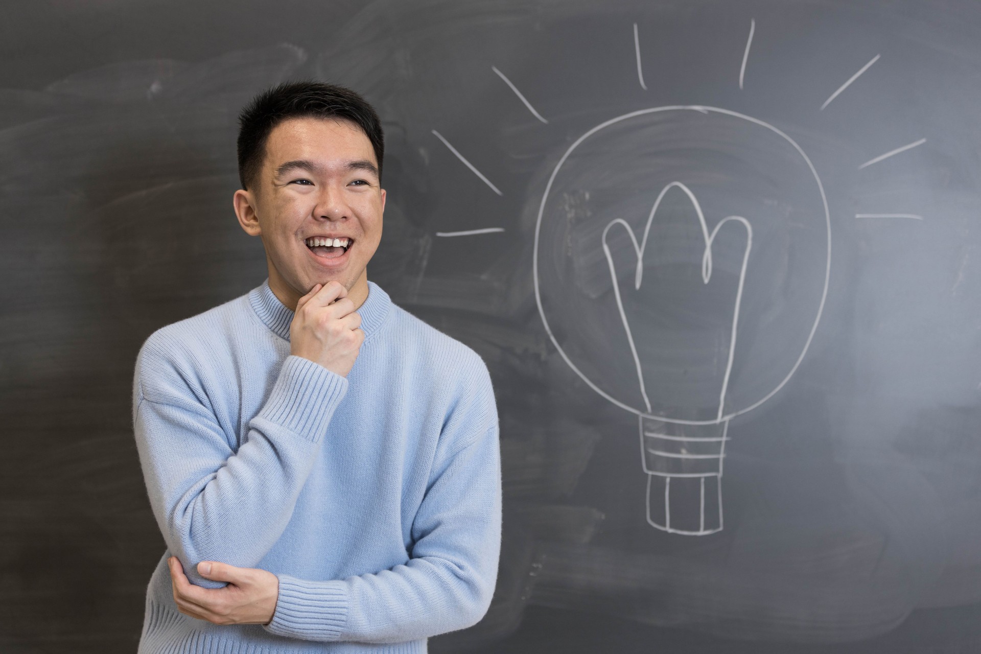 Young student smiling and thinking in front of a blackboard with a lightbulb